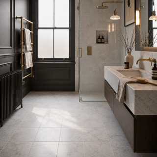 A modern bathroom interior with white grey marble floor and wall tiles, a white marble vanity, dark wood cabinetry, brass fixtures, a glass shower door and a black window with frosted glass.