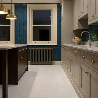 Modern kitchen with blue tiled wall, white cabinets and large off white tiled floor.