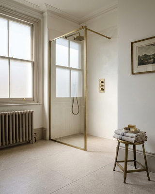 Modern bathroom with a glass shower enclosure, radiator, grigio tiles and stool with towels.