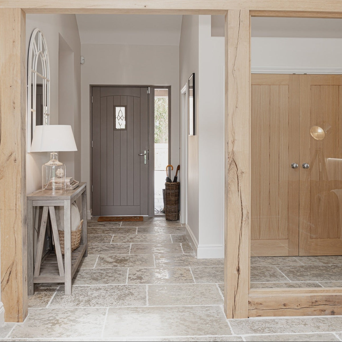 A modern entryway featuring a light natural oak wood frame structure, a gray front door at the end of a tiled hallway, and a matching light oak double door on the right.
